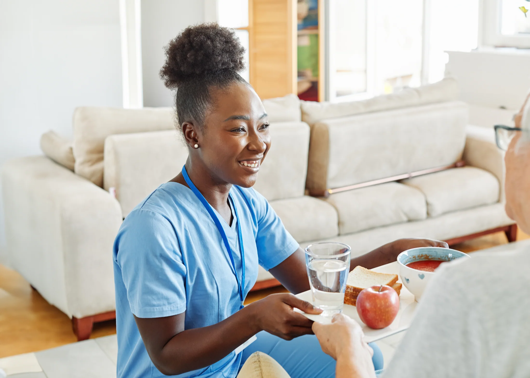Caregiver serving a prepared meal and water to an older adult at home
