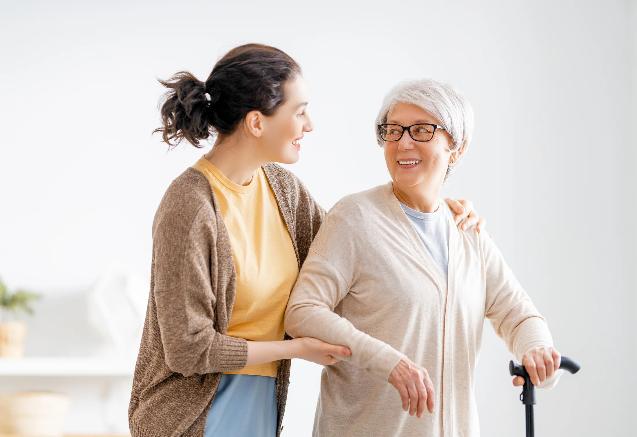 Caregiver supporting an older adult who is walking with a cane