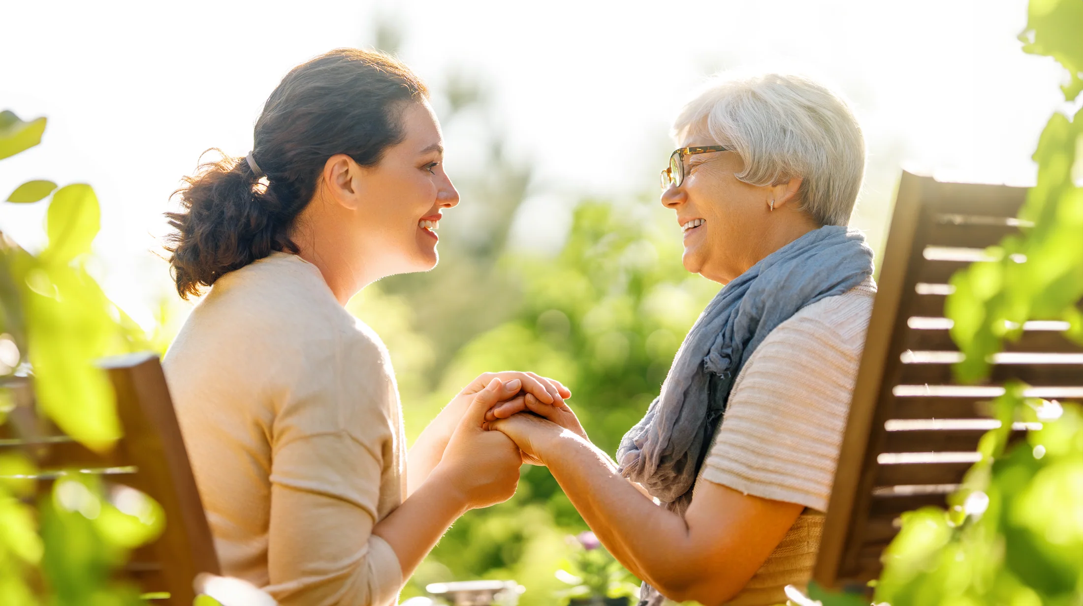 Adult daughter holding her older mother's hand at home